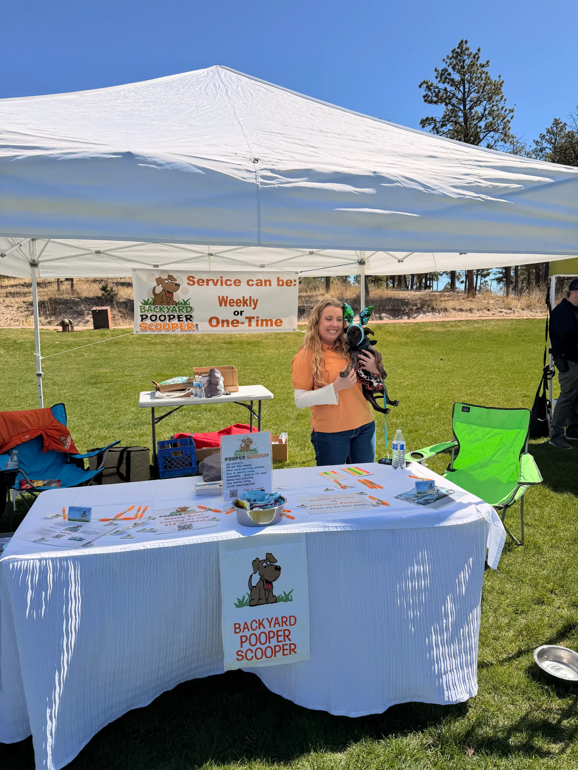 Backyard Pooper Scooper team member holding a small dog at a branded community event booth