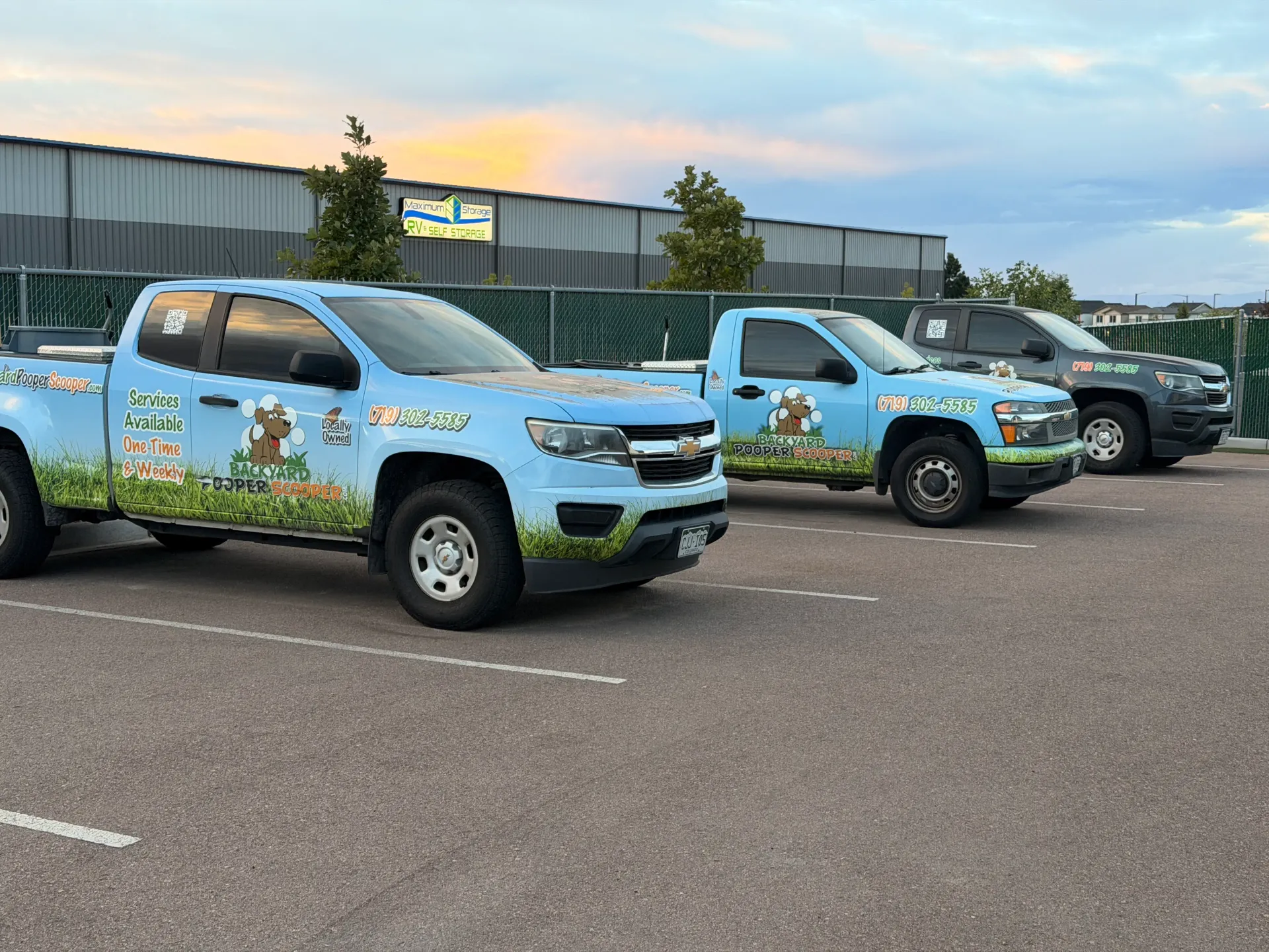 Three light-blue Backyard Pooper Scooper trucks lined up at sunset